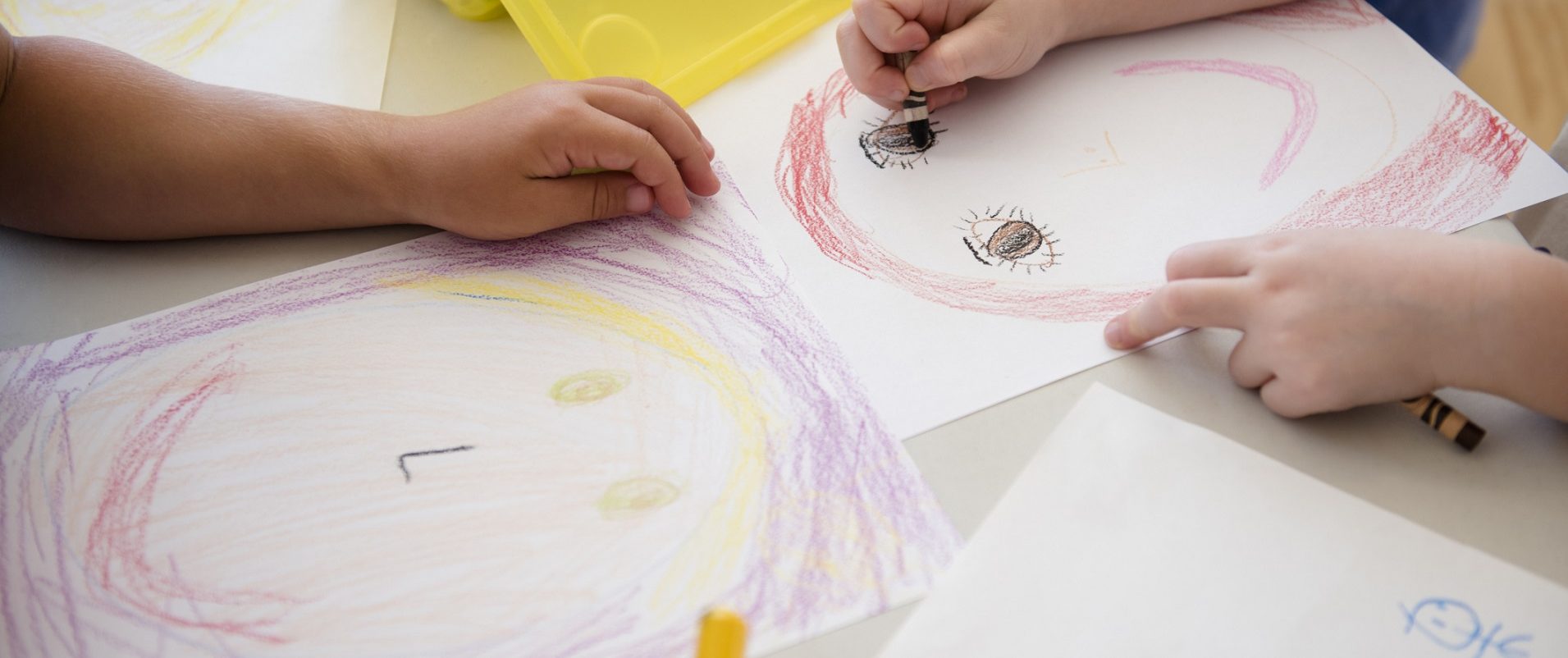 Young children drawing with crayons on paper in a classroom.