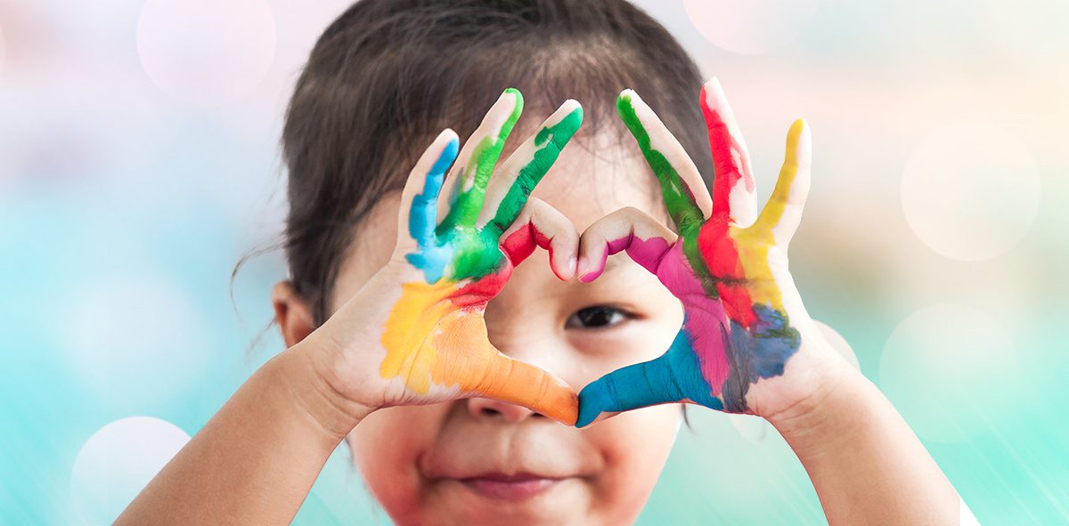 Preschool child making heart with painted hands.
